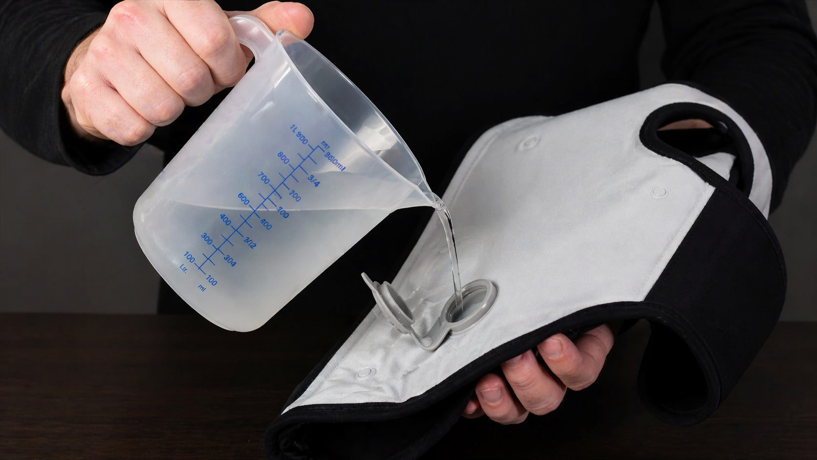 Person pouring liquid from a measuring cup into a dog's cooling vest valve on a dark background